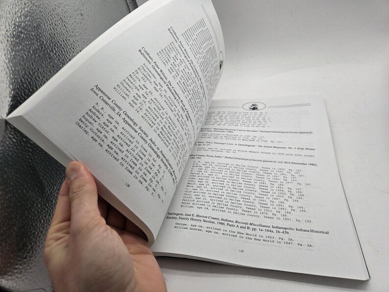 May include: An open book with white pages, featuring printed text. The pages are being turned, revealing more text. The text includes names, ages, and locations. The book appears to be a genealogy or historical reference.