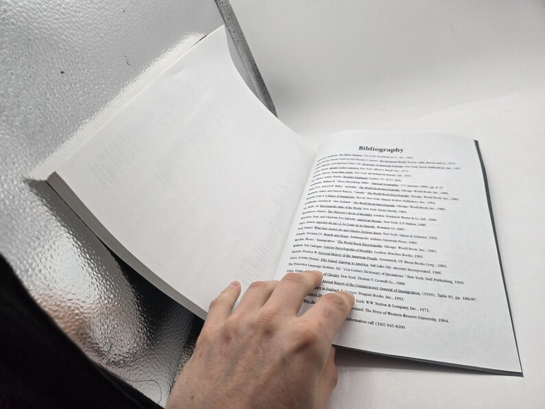 May include: Open book with the title "Bibliography" on the right page. The left page is blank. The book is open, revealing text. The book is held by a hand.
