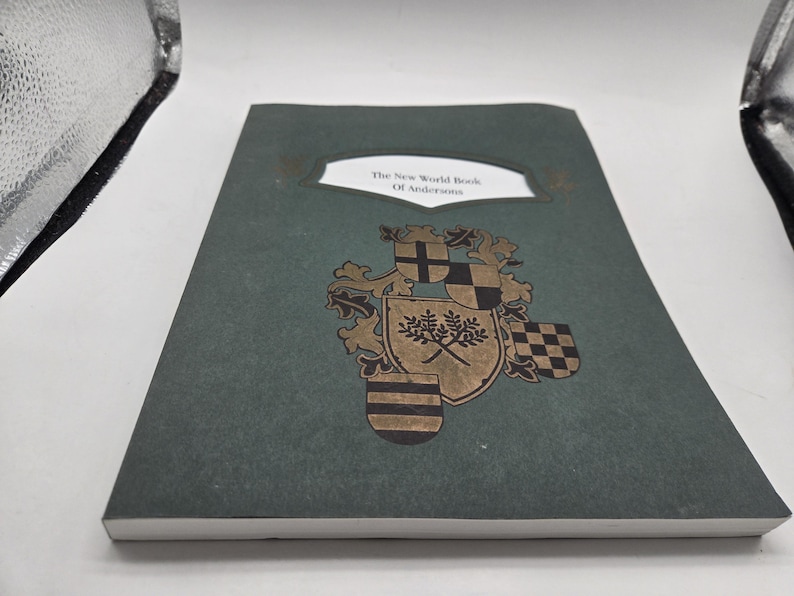 May include: A hardcover book with a dark green cover. The title "The New World Book Of Andersen" is displayed in a white rectangular frame. A gold and black heraldic crest is featured below the title, adding a vintage aesthetic.