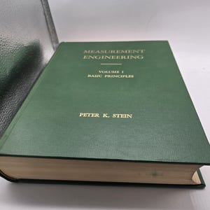 May include: A hardcover book titled "Measurement Engineering, Volume I, Basic Principles" by Peter K. Stein. The book has a dark green cover with gold lettering. The book's pages are off-white.