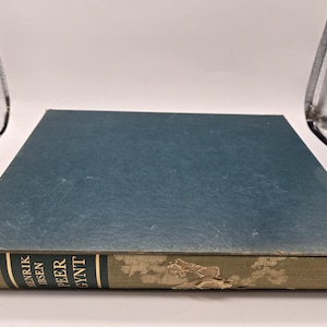 Puede incluir: Un libro de tapa dura azul con letras doradas en el lomo que dice "Henrik Ibsen Peer Gynt".