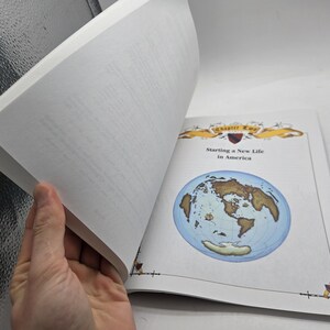 May include: An open book with the title "Starting a New Life in America" and a world map illustration. The book's pages are white, and the cover features decorative elements. A hand is holding the pages open.