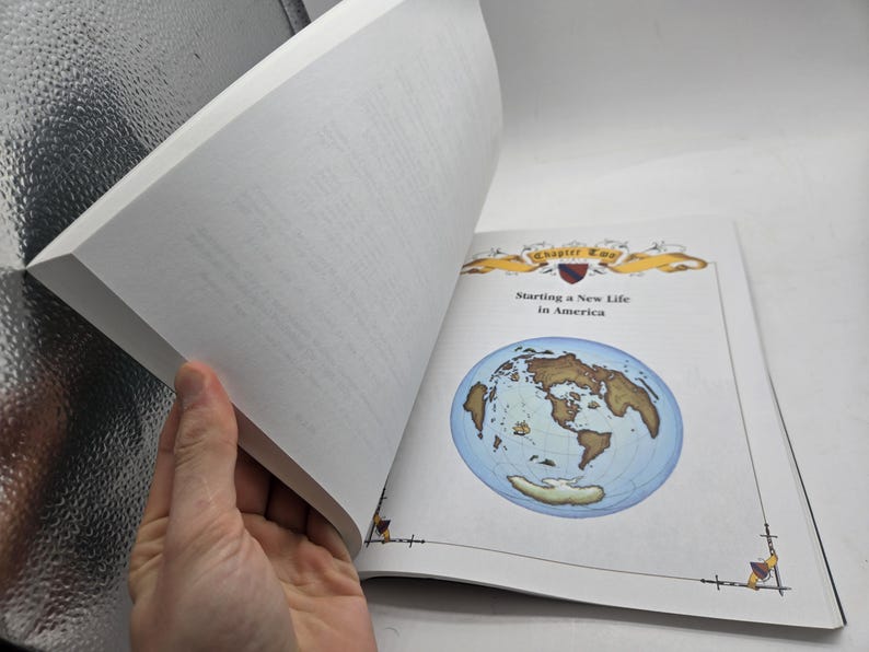 May include: An open book with the title "Starting a New Life in America" and a world map illustration. The book's pages are white, and the cover features decorative elements. A hand is holding the pages open.