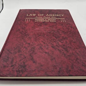 Puede incluir: Un libro color burdeos con el título "Law of Agency" en letras doradas. El libro forma parte de la "American Casebook Series" y está escrito por Warren A. Seavey y Livingston Hall.