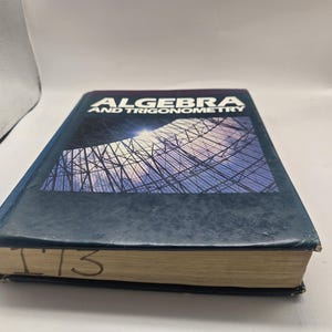 May include: A hardback textbook titled Algebra and Trigonometry with a dark blue cover featuring a graphic of a structural dome. The book has visible wear on the edges and the number 173 is handwritten in black ink on the bottom page edges.
