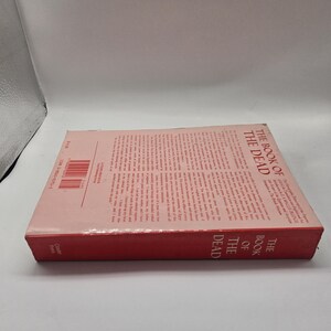 Puede incluir: Un libro de tapa dura titulado "The Book of the Dead" con lomo rojo y cubierta rosa claro. El t&iacute;tulo del libro est&aacute; impreso verticalmente en el lomo. La portada presenta texto impreso y un c&oacute;digo de barras.