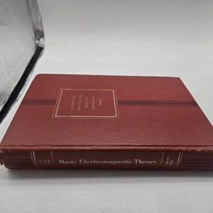 May include: A hardcover book with a maroon cover. The title "Basic Electromagnetic Theory" is printed in gold on the spine. The book has a rectangular gold label on the front cover with text. The book is closed and lying flat.