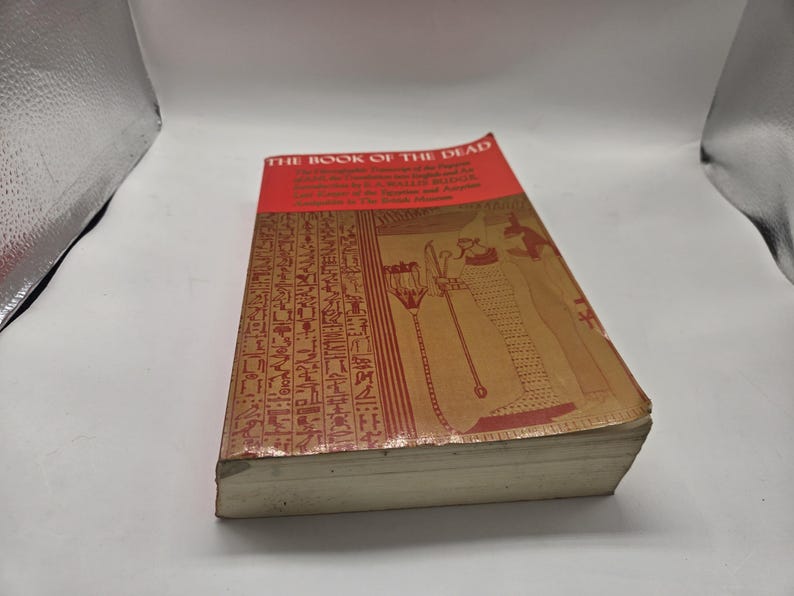 Puede incluir: Un libro antiguo titulado "THE BOOK OF THE DEAD" con una cubierta roja y marr&oacute;n. La cubierta presenta jerogl&iacute;ficos e ilustraciones en marr&oacute;n y rojo. Las p&aacute;ginas del libro est&aacute;n envejecidas y el lomo muestra desgaste.