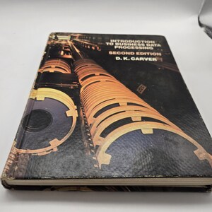May include: A hardcover book titled "Introduction to Business Data Processing, Second Edition" by D.K. Carver. The cover features a dark background with a graphic of cylindrical structures in shades of orange and black.
