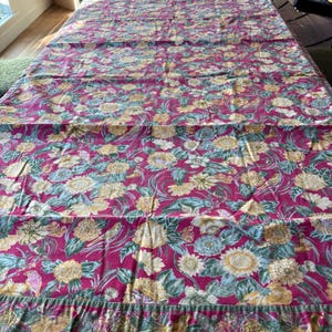 May include: A rectangular fabric textile featuring a deep magenta background with a dense, repeating pattern of yellow sunflowers, light blue flowers, and green foliage. The design includes small bird illustrations interspersed throughout the floral print.