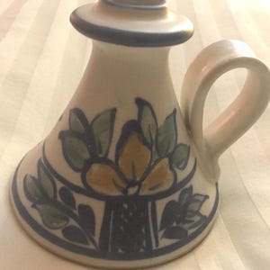 May include: A white ceramic candle holder with a blue and green floral design. The holder has a handle and a wide base.