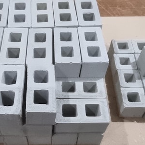 Könnte beinhalten: Eine Sammlung grauer Betonblöcke mit einem quadratischen Loch in der Mitte jedes Blocks. Die Blöcke sind in einer rechteckigen Form gestapelt.