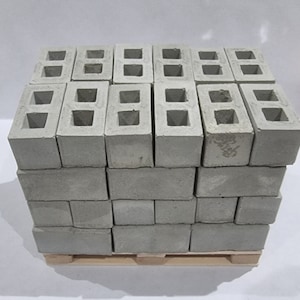 May include: A stack of grey concrete breeze blocks on a wooden pallet. The blocks have two holes in each.