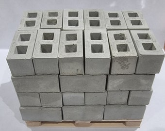 Puede incluir: Una pila de bloques de hormigón gris sobre una plataforma de madera. Los bloques tienen dos agujeros cada uno.