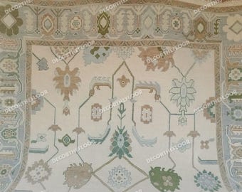 May include: A white rug with a beige, green, and blue floral pattern. The rug has a border with a repeating pattern.