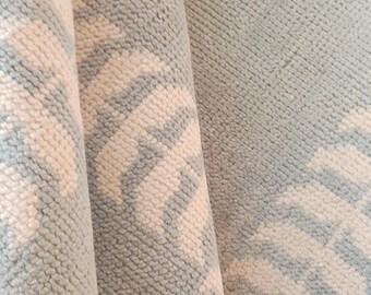 May include: Close-up of a light blue rug with a white patterned design. The rug has a soft, textured surface.
