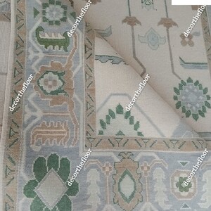 Puede incluir: Primer plano de una alfombra beige con un patr&oacute;n geom&eacute;trico en tonos de verde, marr&oacute;n y gris. La alfombra tiene un borde de flecos y est&aacute; doblada por la mitad.