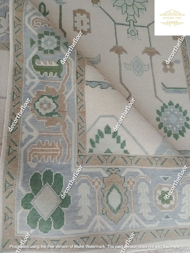 Puede incluir: Primer plano de una alfombra beige con un patr&oacute;n geom&eacute;trico en tonos de verde, marr&oacute;n y gris. La alfombra tiene un borde de flecos y est&aacute; doblada por la mitad.