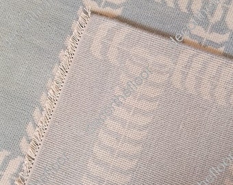 May include: A close-up of a light blue rug with a white geometric pattern. The rug has a fringe border and is folded in half.