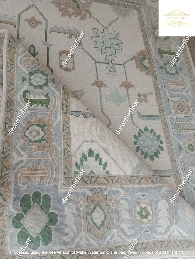 Puede incluir: Una alfombra beige con un patr&oacute;n geom&eacute;trico azul claro y verde. La alfombra tiene una esquina doblada, revelando la parte inferior de la alfombra.