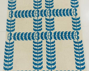 May include: A rectangular area rug featuring a cream-colored base with a repeating blue geometric pattern of vertical and horizontal lines composed of stylized leaf-like shapes. The rug is finished with short, cream-colored fringe on both ends.