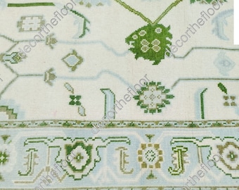 May include: A white rug with a green and blue floral pattern. The rug has a light blue border with a green and brown design.