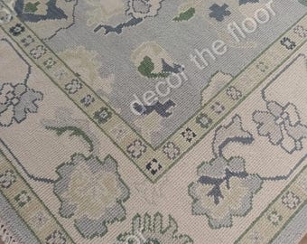 Puede incluir: Una alfombra de color azul claro y crema con un patrón floral. La alfombra tiene un borde de flecos.
