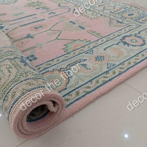 Puede incluir: Una alfombra de color rosa y azul con un borde verde y blanco está enrollada. La alfombra está hecha de un material suave y tejido.