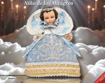 Puede incluir: Muñeca vestida con un vestido bordado en azul claro y dorado, con un halo blanco y azul. La muñeca tiene una expresión serena y está situada sobre un fondo de nubes y luz suave. El texto "Niño de los Milagros" está en la parte superior.
