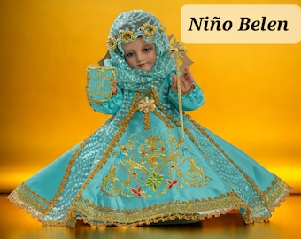 Puede incluir: Una muñeca vestida con un vestido azul y dorado con una corona y una varita con forma de estrella. La muñeca sostiene un cartel que dice "Niño de Belen".