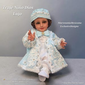 May include: A light blue and white outfit for a doll, featuring a matching cap, a long-sleeved jacket with intricate white lace and sequin embellishments, a bow tie, and white trousers. Text reads: Traje Niño Dios Lujo, NlartesaniaMexicana ExclusiveDesigns.