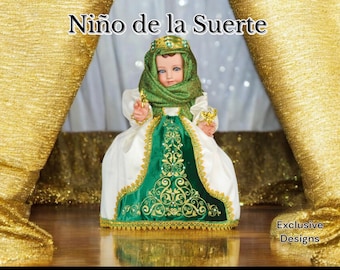 Puede incluir: Una muñeca vestida con un vestido blanco y verde con ribetes dorados. La muñeca lleva un chal verde y una corona. La muñeca está de pie sobre una superficie dorada y blanca. El texto "Niño de la Suerte" está por encima de la muñeca. El texto "Exclusive Designs" está por debajo de la muñeca.