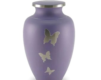 May include: A lavender urn with a silver lid and base. Three silver butterfly silhouettes are displayed on the front of the urn. The urn has a classic, rounded shape, suitable for memorializing a loved one.