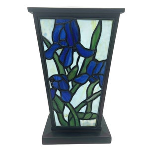 May include: A stained glass lamp with a dark brown frame and base. The lamp features a design of blue iris flowers with green leaves against a white background. The lamp is approximately 12 inches tall.