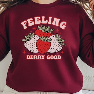 Può includere: Felpa bordeaux con la scritta "FEELING BERRY GOOD" e una grafica di fragole. Le fragole sono rosse e bianche con foglie verdi. La felpa è di colore bordeaux unito.