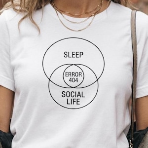 May include: A white short-sleeved t-shirt featuring a black graphic of a Venn diagram. The top circle is labelled SLEEP, the bottom circle is labelled SOCIAL LIFE, and the centre intersection contains the text ERROR 404 in black capital letters.