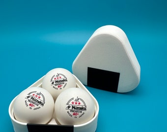 May include: Three white table tennis balls in a white and black container. The balls have red lettering that says "Nittaku Premium 40+ Made in Japan".
