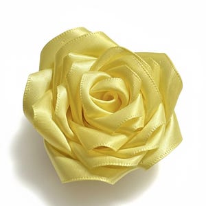 May include: A handcrafted yellow satin rose, a floral embellishment. The flower is made from meticulously arranged ribbon, creating a realistic rose shape. The petals are a soft yellow hue, perfect for crafts or accessories.