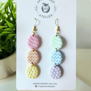 May include: Pastel colored polymer clay earrings with a variety of patterns. The earrings are displayed on a white card with the text "Appleseed Atelier" and the shop's website and Instagram handle.