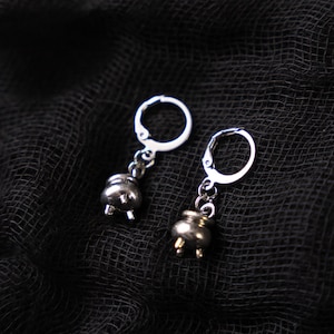 May include: A pair of silver earrings with a cauldron charm. The charms are detailed and have a three-dimensional look.