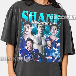 Może przedstawiać: Ciemnoszary t-shirt z krótkim rękawem z nadrukiem graficznym Shane'a Hollandera. Wzór zawiera cztery zdjęcia tej samej osoby, w tym jedno bez koszulki i dwa w strojach hokejowych, na tle niebieskich błyskawic.