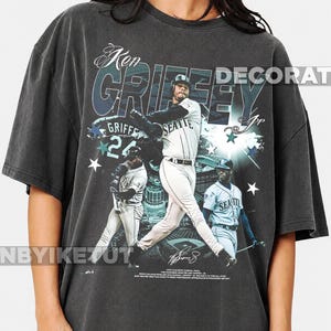 May include: A charcoal grey oversized t-shirt featuring a graphic print of baseball player Ken Griffey Jr. in a Seattle uniform. The design includes multiple images of the player, the text Ken Griffey Jr., the number 24, and star accents.