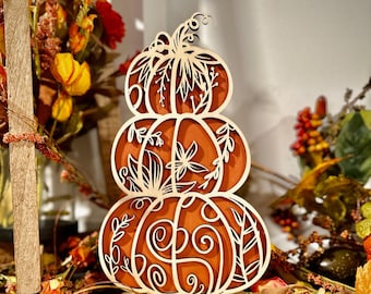 May include: A three-tiered wooden pumpkin decoration with intricate cut-out designs. The pumpkin is orange with a light wood overlay, featuring floral and swirl patterns. It sits on a wooden base, perfect for fall decor.