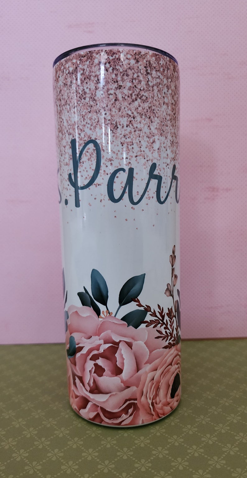 Pu&ograve; includere: Un bicchiere bianco con un design glitter rosa e un motivo floreale. Il bicchiere ha il nome "Parr" scritto in nero.