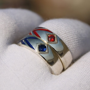 May include: Two silver rings with blue and red enamel and gemstones. The rings are stacked on top of each other.