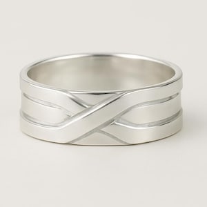 Pode incluir: Um anel de prata com um design único. O anel apresenta uma série de faixas horizontais com um padrão entrelaçado na frente. O anel é feito de um material metálico brilhante.