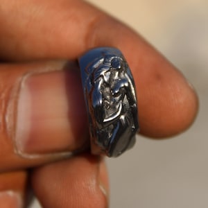 May include: A silver ring with a detailed design of two figures intertwined.