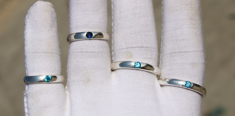 May include: Four silver rings with blue gemstones. The rings are displayed on a white surface.