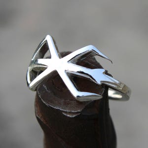 Op de afbeelding: Een zilveren ring met een geometrisch ontwerp. De ring is gemaakt van één stuk metaal en heeft een gladde afwerking.