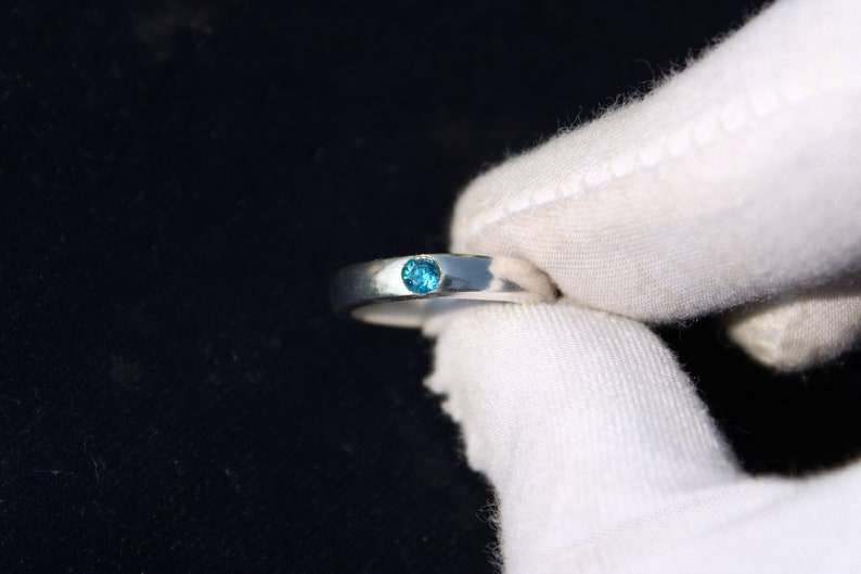 May include: A silver ring with a small, round, blue gemstone set in the center.